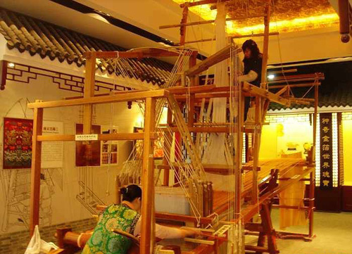 Two ladies are weaving by wooden traditional Chinese equipment.